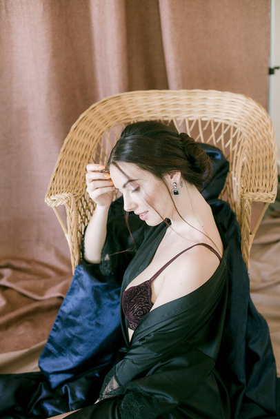 Young attractive girl with dark hair in a black silk robe in a boudoir setting. Beauty and Fashion - Foto, imagen