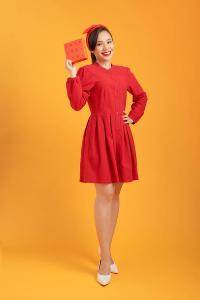 Happy young Asian woman holding gift box isolated over orange background. - 写真・画像