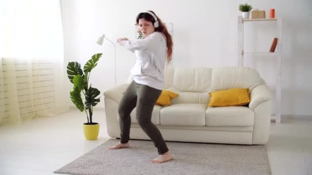 Happy woman listening to music and dancing in living room - Záběry, video
