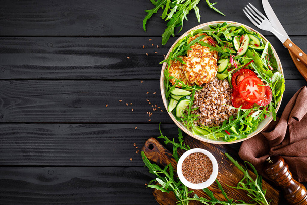 Lunch bowl with buckwheat porridge, fried chicken cutlets and fresh vegetable salad of arugula, lettuce, chard leaves, tomato, cucumber and flax seeds - Фото, изображение
