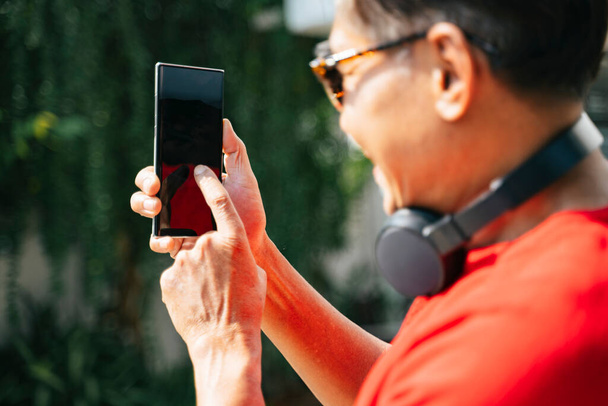 Обрезанный iamge смартфона в руках старика, пока он выбирает музыку из приложения
. - Фото, изображение