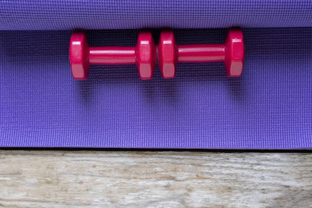 red dumbbell and yoga mat on wooden table, fitness healthy and sport concept - Foto, afbeelding