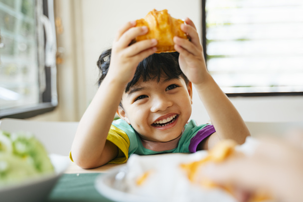 Счастливый маленький мальчик наслаждайтесь завтраком, колбасные круассаны и салат
. - Фото, изображение