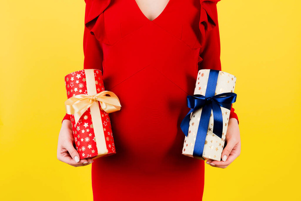 Cropped image of pregnant woman in red dress holding two gift boxes at yellow background. Is it a boy or a girl Waiting for twins. Pregnancy celebration. Copy space. - Fotografie, Obrázek
