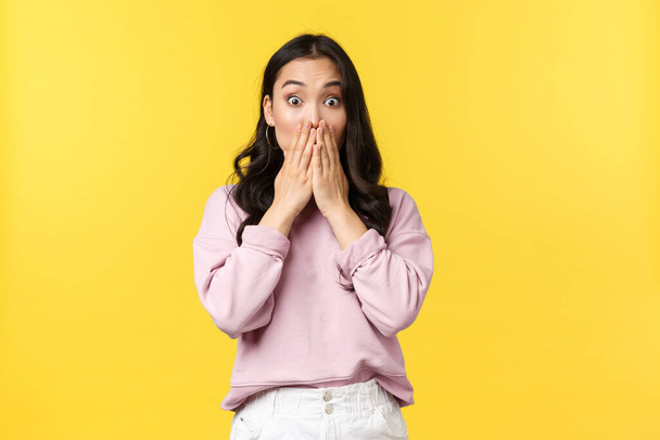 People emotions, lifestyle and fashion concept. Concerned and startled, shocked korean girl in casual outfit, gasping cover mouth hands and look in panic, cant believe own eyes, yellow background - Foto, Bild