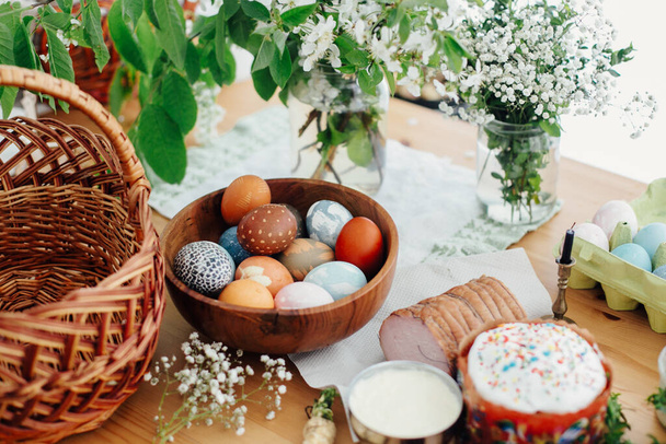 Easter eggs natural dyed, easter bread cake, ham, butter, green branches  and flowers on rustic wooden table with wicker basket and candle. Traditional Easter Food for blessing in church - Fotografie, Obrázek