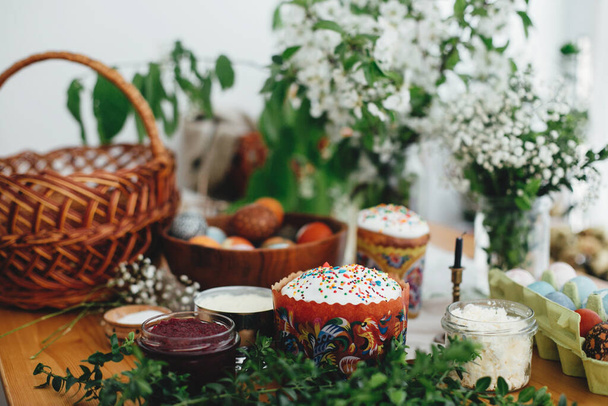 Wielkanoc domowe ciasto, buraki, jajka naturalne barwione, szynka,, masło, zielone gałęzie i kwiaty na rustykalnym drewnianym stole z wiklinowym koszem i świecą. Tradycyjne wielkanocne jedzenie dla błogosławieństwa w kościele - Zdjęcie, obraz