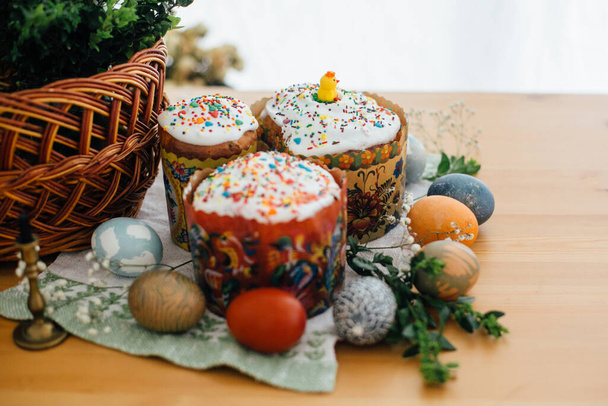 Traditional Easter food on rustic table. Homemade easter cake, easter eggs natural dyed, candle, green branches and flowers with wicker basket on wooden background. Easter Food for sanctify - Φωτογραφία, εικόνα