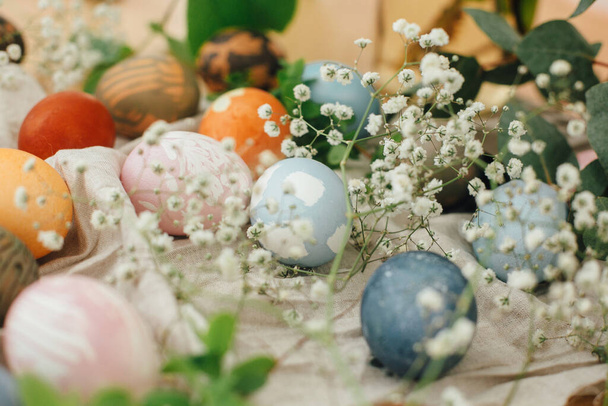 素朴な背景に天然染料で描かれた現代の最小限の装飾品とイースターの卵。春の花や緑の枝を持つ木製のテーブルの上にスタイリッシュなカラフルなイースターエッグ。廃棄物ゼロ休日 - 写真・画像