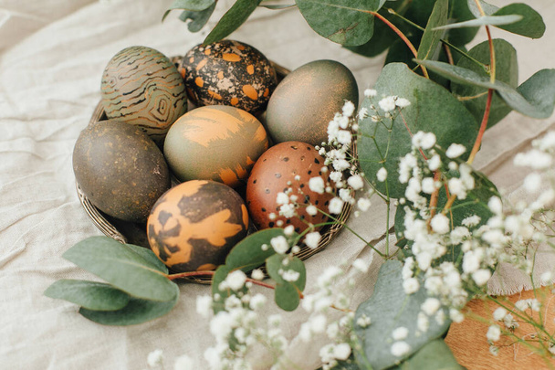 Oeufs de Pâques modernes avec fleurs de printemps et eucalyptus sur table en bois rustique. Élégantes pierres grises et œufs de Pâques verts peints dans un colorant naturel à base de thé carcade. Joyeuses Pâques. - Photo, image