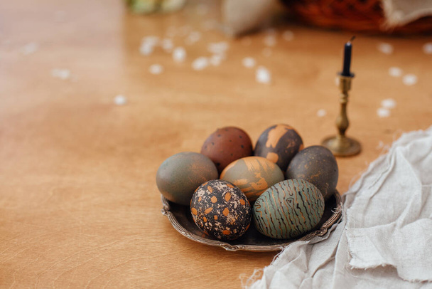 Huevos de Pascua modernos en plato vintage sobre mesa de madera rústica con vela. Elegante piedra gris y huevos verdes de Pascua pintados en tinte natural de té de carcade. Feliz Pascua
 - Foto, Imagen
