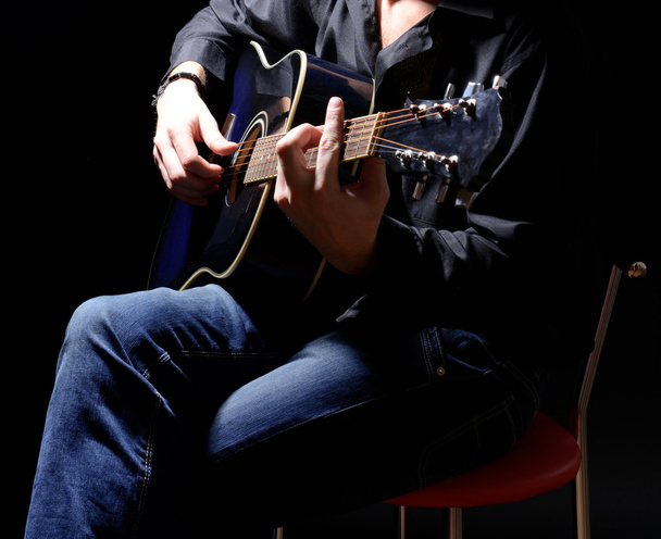 Young musician playing acoustic guitar and singing, on dark background - Fotografie, Obrázek