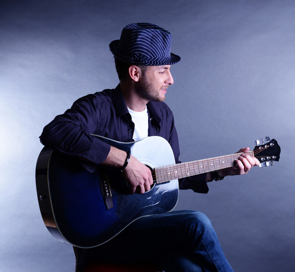 Young musician playing acoustic guitar and singing, on gray background - Foto, Imagen