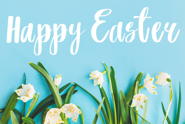 Joyeux texte de Pâques sur les fleurs blanches du printemps sur un plat bleu vif. Carte de vœux créative de Pâques élégante. Salutations de Pâques. Bannière avec lettrage - Photo, image