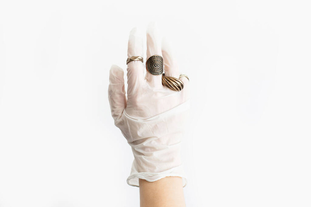 Mode und Quarantäne. Hand in weißer medizinischer Handschuh mit modernen Ringen an den Fingern auf weißem Hintergrund. Hautschutz, Vorbeugung gegen Viren mit Stil. Positive Stimmung während der Epidemie. - Foto, Bild