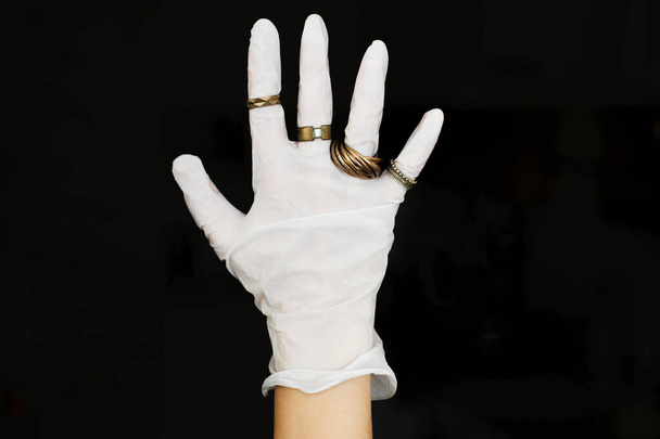 Guante médico mano en blanco con anillos modernos en los dedos sobre fondo negro. Moda y cuarentena. Protección de la piel, prevención de virus en el estilo. Vibraciones positivas durante la epidemia. Idea creativa
 - Foto, imagen