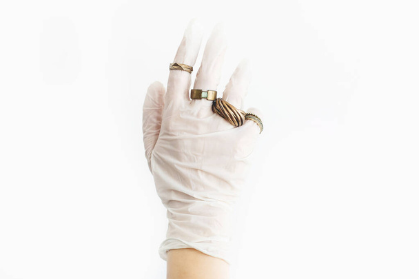 Hand in hand witte medische handschoen met moderne ringen op vingers op witte achtergrond. Mode in virusepidemie. Huidbescherming, preventie van virussen in stijl. Positieve vibes in quarantaine - Foto, afbeelding