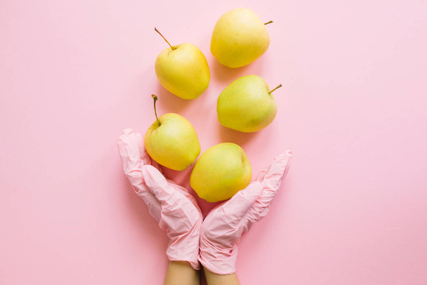 Kädet vaaleanpunainen käsine tilalla omenat vaaleanpunainen tausta tasainen lay. Tilaa ostokset ja toimita ne turvallisesti karanteenin aikana. Pysy kotona. Pysy turvassa. Virusepidemian ehkäisy. Puhdas ruoka - Valokuva, kuva