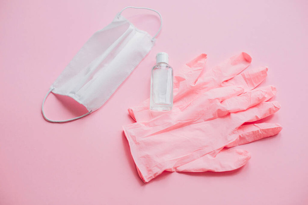Pink gloves, face mask, disinfectant bottle on pink background flat lay. Stay safe. Prevention of virus epidemic. Antiseptic alcohol gel for hands. Safe shopping and walking outside in quarantine - Photo, Image