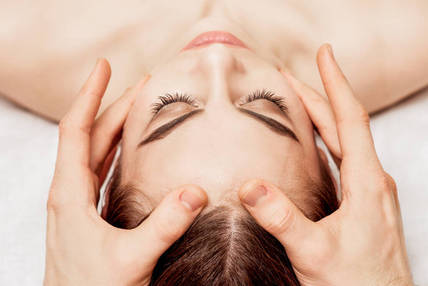 close-up jonge vrouw ontvangst hoofd massage door handen van massage therapeut. - Foto, afbeelding