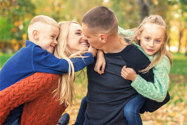 Retrato de una joven familia jugando en el parque de otoño. Padres besándose y descansando con los niños en el parque de otoño - Foto, Imagen