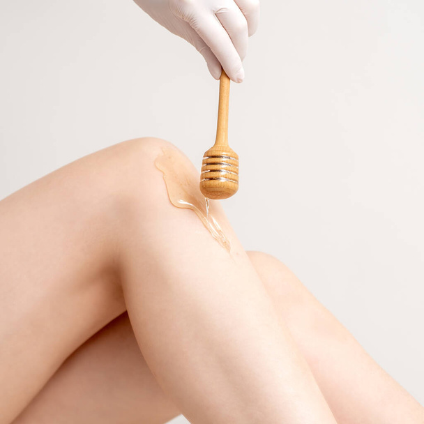 Wax on honey stick flowing down on female leg in human hand wearing protective glove on white background - Photo, Image