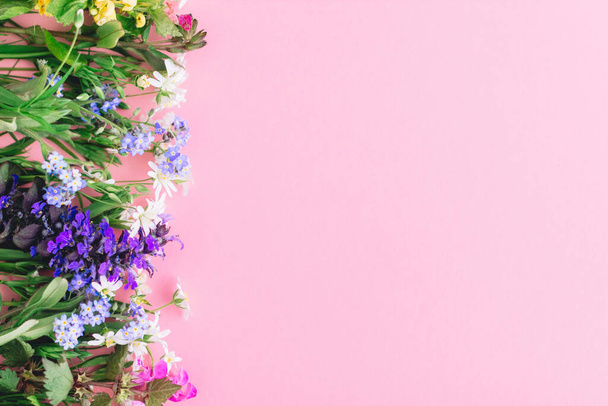 Bloemen vlakke lay van kleurrijke lente wilde bloemen op roze papieren achtergrond, ruimte voor tekst. Bloemen wenskaart template. Gelukkige Moederdag concept. Hallo lente. Bloeiende lente bloemen grens - Foto, afbeelding