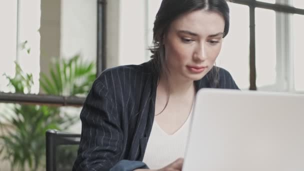 A good-looking young businesswoman is working with her laptop computer while sitting in the office - Materiał filmowy, wideo