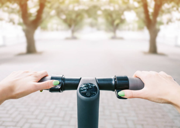 Young woman riding an electric scooter in summer park, point of view in first person of handlebar and hands. - Photo, Image