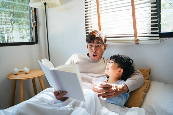 Old man with gray hair tell the bedtime story for his grandson for daytime sleep. - 写真・画像