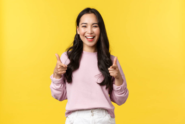 People emotions, lifestyle and fashion concept. Enthusiastic and friendly smiling pretty girl pointing fingers at camera, praising nice job, picking you, complimenting, yellow background - Photo, Image