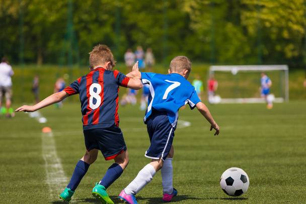 Two youth football players running in duel after ball. Kids kicking soccer match on the grass field. School children in sports jersey  clothes with numbers on back in tough competition - Fotoğraf, Görsel
