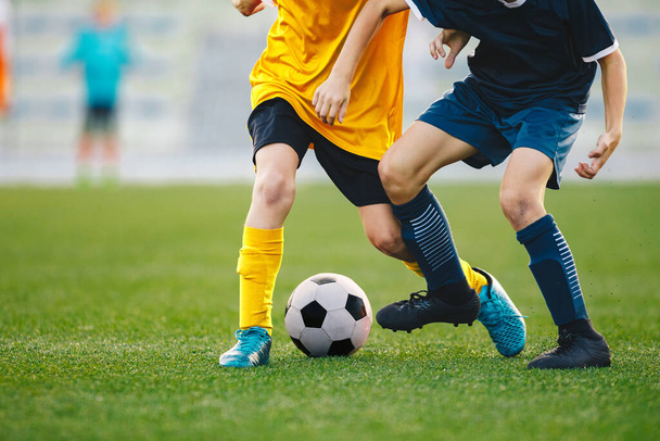 Крупный план ног футболистов в поединке. Мальчики пинают футбольный мяч по траве. Момент соревнования между двумя молодыми футболистами
 - Фото, изображение