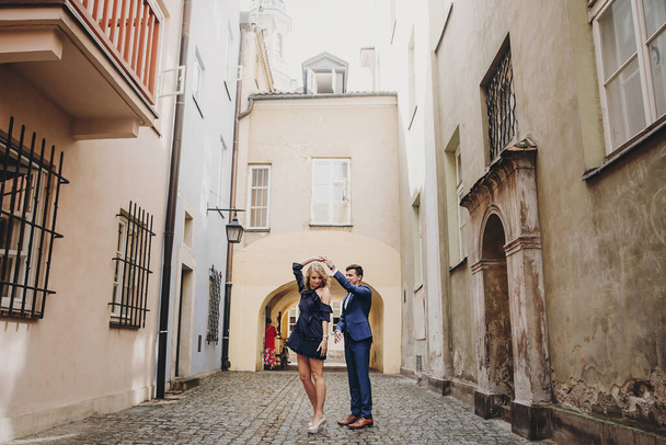 Stylish couple dancing in european city street on background of old architecture. Fashionable man and woman in love dancing with passion in city. Traveling together in Europe - Фото, зображення