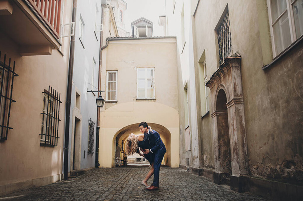 Stylish couple dancing in european city street on background of old architecture. Fashionable man and woman in love dancing with passion in city. Traveling together in Europe - Φωτογραφία, εικόνα