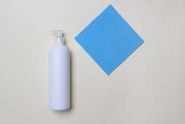 botella blanca con agente de limpieza y servilleta azul sobre fondo blanco vista superior
. - Foto, imagen