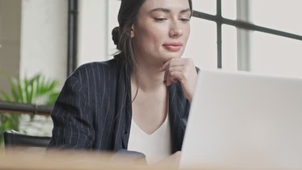 An attractive young businesswoman is using her laptop computer while working in the office - Imágenes, Vídeo