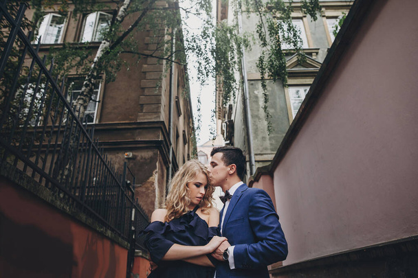 Κομψό ζευγάρι αγκαλιάζει και φιλιά σε ευρωπαϊκό δρόμο της πόλης. Αισθησιακή παθιασμένη στιγμή. Μοντέρνος άντρας και γυναίκα ερωτευμένοι αγκαλιάζονται απαλά. Ημέρα του Αγίου Βαλεντίνου - Φωτογραφία, εικόνα