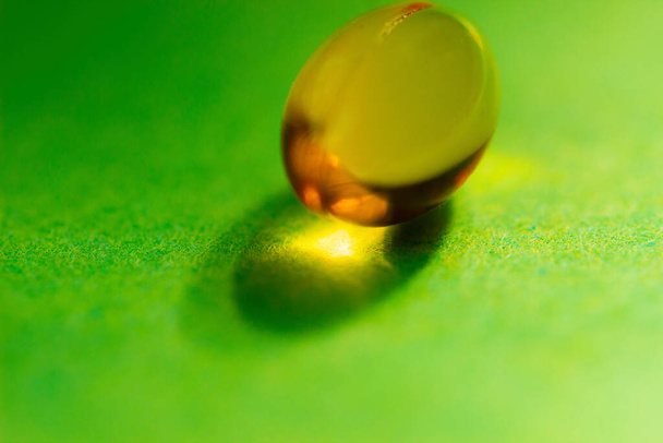 una cápsula amarilla grande sobre un fondo verde. el concepto de deficiencia o consumo excesivo de vitaminas para la salud del cuerpo
. - Foto, Imagen