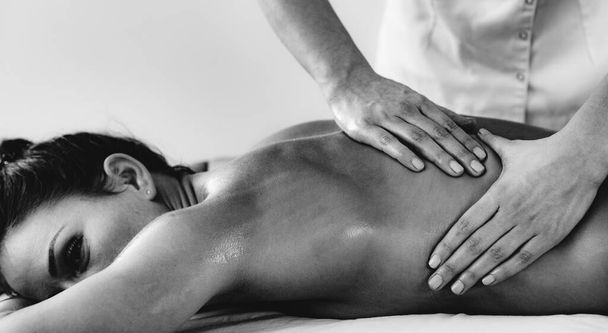 Physiotherapist massaging female patient with injured back muscle. Sports injury treatment. - 写真・画像