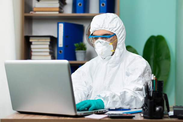 Człowiek dezynfekcja ze specjalnym białym apartamentem pracy na laptopie w biurze - Zdjęcie, obraz