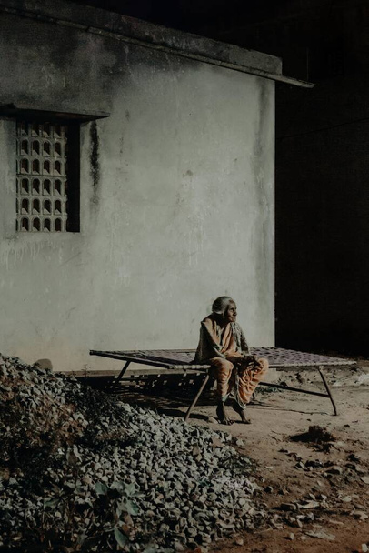 BANGALORE, INDIA - 12 nov 2019: Een oude dame die 's nachts onder een straatlantaarn in een dorp zit - Foto, afbeelding