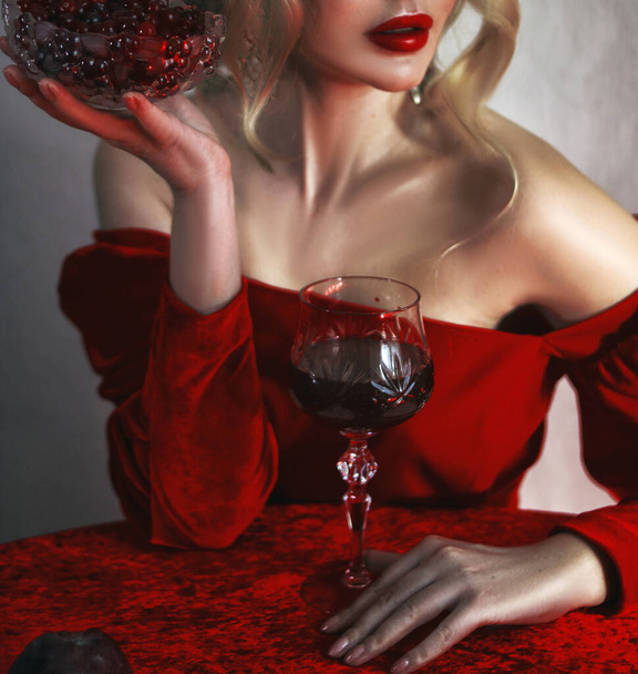 A girl in a red dress sits at a red table with a glass of red wine and holds in her hand a plate with red berries - Foto, Imagen