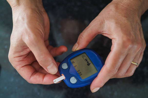 Medicine, Diabetes, Glycemia, Health care and people concept - close up of female using lancelet on finger to checking blood sugar level by Glucose meter - Photo, Image