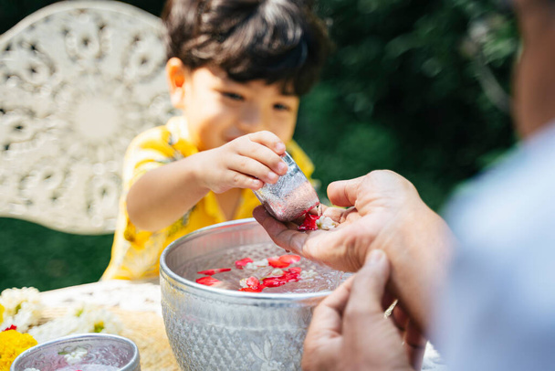 Petit garçon verser l'eau avec des fleurs sur la main de son grand-père comme une tradition au jour de Songkran. - Photo, image