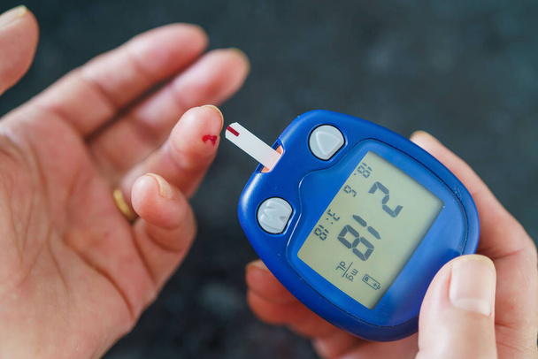 Medicine, Diabetes, Glycemia, Health care and people concept - close up of female using lancelet on finger to checking blood sugar level by Glucose meter - Photo, Image
