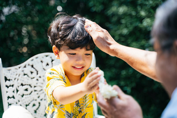 Το αγοράκι έδωσε στον παππού του το γιασεμί γιασεμί αφού έχυσε το χέρι του παππού ως προϋπόθεση, ο παππούς έτριψε απαλά το κεφάλι του.. - Φωτογραφία, εικόνα