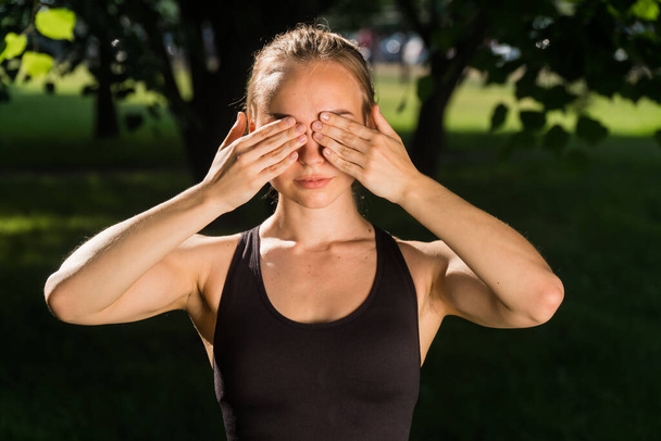 Portrait of a stylish young girl in sports fitness clothes with a closed face palm, against the backdrop of a green park on a fresh cheer - Fotografie, Obrázek