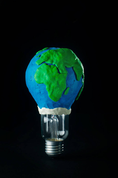 Earth Hour concept: electric lamp decorated as plasticine Earth planet model on black background with blank space for text - Fotografie, Obrázek