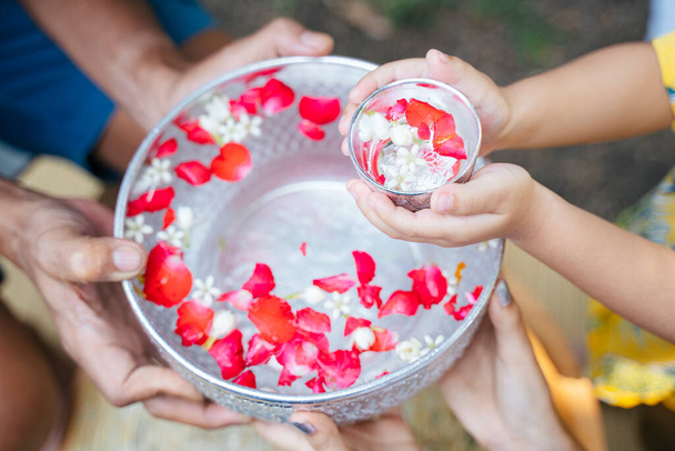 Καλλιεργημένη εικόνα εναέρια λήψη των χεριών και ασημί μπολ με floral νερό στην παραδοσιακή ημέρα. - Φωτογραφία, εικόνα